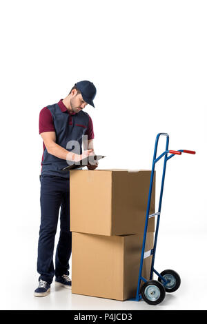 L'homme en uniforme de livraison contrôle de notes dans le bloc-notes avec des boîtes en carton sur camion de main près de par isolated on white Banque D'Images