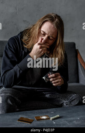 L'inhalation de l'homme dépendant de la cocaïne alors qu'il était assis sur la table Banque D'Images