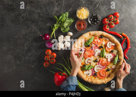 Cropped shot of woman putting olives noires sur la pizza italienne sur la table sombre Banque D'Images