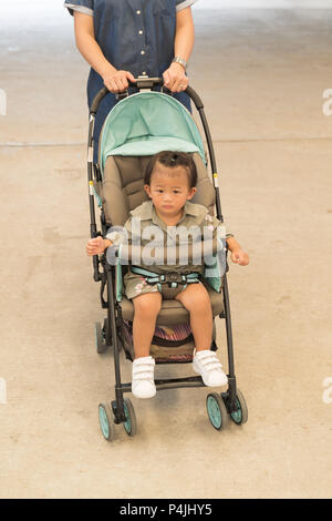 Asian cute baby girl antennes en poussette avec maman prendre soin de l'extérieur de l'arrière-plan. Banque D'Images