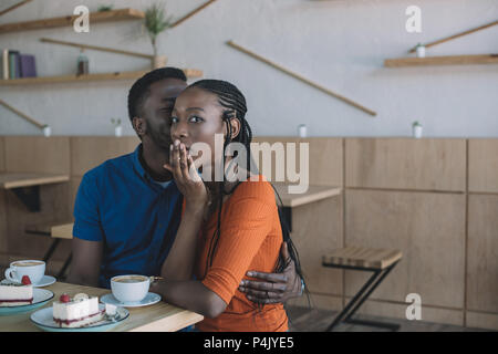 African American man secret dit choqué de petite amie à table dans cafe Banque D'Images