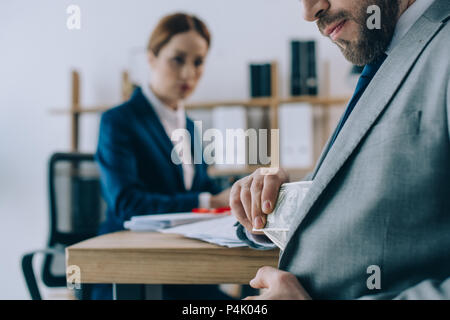 Focus sélectif de businessman taking billets en dollars de votre poche avec collègue sur le lieu de travail derrière in office Banque D'Images