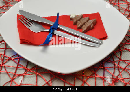 Un endroit simple définition pour Noël composé d'une assiette, fourchette, couteau, serviette rouge et un chocolat Christmas Tree sur un set de table rouge Banque D'Images