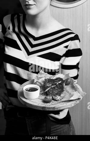 Femme vêtue de la tenue de cavalier à rayures avec plaque en bois jeu appétissant servi avec des tomates cerises, sauce romarin et couché sur morceau de kra Banque D'Images