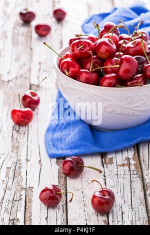 Un bol de cerises fraîches sur un tissu bleu sur une table en bois patiné Banque D'Images