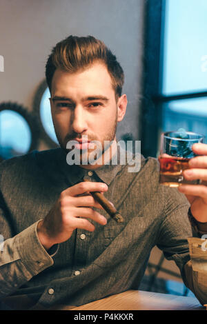 Portrait de jeune homme avec le verre de cognac et cigare dans mains in cafe Banque D'Images