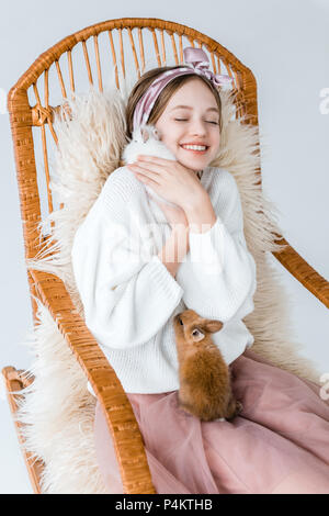 Beautiful happy woman hugging lapins tout en restant assis dans un fauteuil à bascule sur blanc Banque D'Images