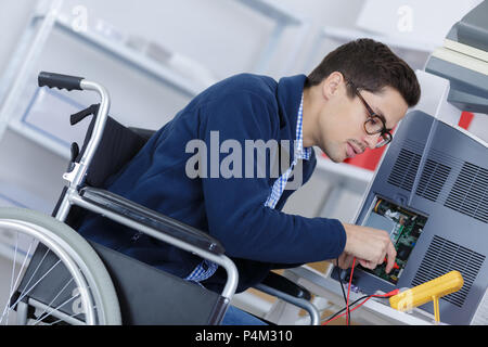 L'homme à l'appareil d'essais en fauteuil roulant avec un multimètre Banque D'Images