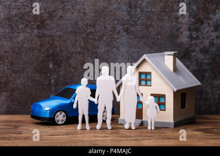 Figures humaines debout devant de la maison et de la voiture bleue sur planche en bois Banque D'Images