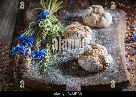 Petits pains complets sains avec des épis de maïs et de fleurs des champs sur une planche en bois Banque D'Images