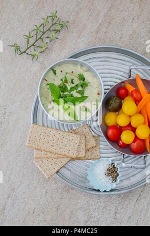 Herb houmous sur un plateau avec des tomates et pain croustillant. Banque D'Images