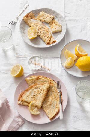 Deux plaques de plié et crêpes roulées avec des quartiers de citron sur des draps blancs couverts table et verres à eau Banque D'Images