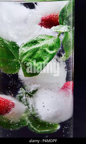 Des cubes de glace avec des framboises et de basilic dans un verre d'eau Banque D'Images