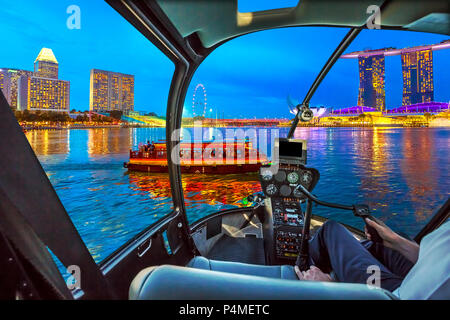 Pilotage d'hélicoptère en vol d'intérieur sur Singapour panorama sur les bâtiments gratte-ciel et la grande roue reflète dans la mer. Bateau de croisière touristique voiles dans la baie de soirée. Singapour waterfront skyline dusk. Banque D'Images