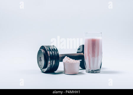 Whey Protein Shake dans un verre à côté de rase de poudre et l'haltère sur un fond blanc. Nutrition Fitness boisson et des poids lourds. Banque D'Images