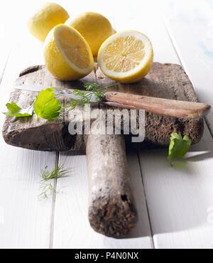 Les citrons coupés en deux sur une vieille planche de bois avec persil, aneth et un couteau Banque D'Images