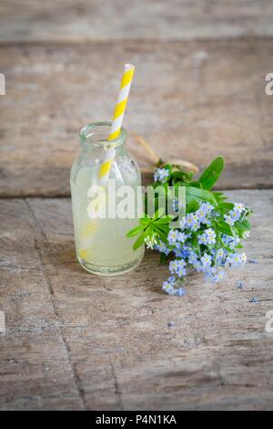 Limonade à la rhubarbe dans une mini bouteille en verre à côté d'un bouquet de myosotis Banque D'Images
