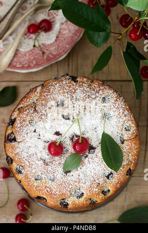 Cherry pie, saupoudré de sucre en poudre sur une table en bois sur fond de branches de cerisier. De style rustique, selective focus. Banque D'Images