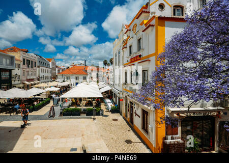 Cascais, Portugal - 8 juin 2018 : bars et restaurants touristiques avec l'architecture traditionnelle portugaise et bleu sur le premier plan d'arbres Jacaranda Banque D'Images