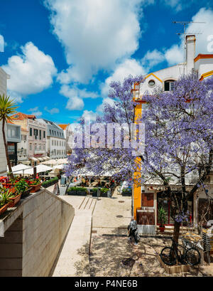 Cascais, Portugal - 8 juin 2018 : bars et restaurants touristiques avec l'architecture traditionnelle portugaise et bleu sur le premier plan d'arbres Jacaranda Banque D'Images