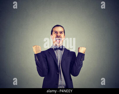 Formelle excité man in suit holding poings et célébrer la réussite et nouvelle réalisation criant sur fond gris Banque D'Images