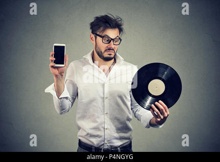 Jeune homme barbu dans les verres à la perplexe tout en choisissant entre les disques vinyle et smartphone Banque D'Images