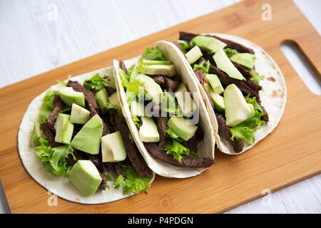 Trois tacos mexicains sur le conseil de bambou sur un fond de bois blanc. Libre. Banque D'Images