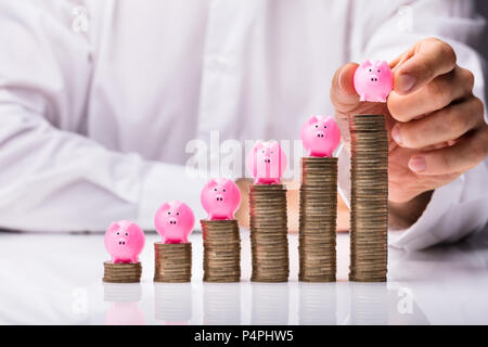 Close-up of a person's Hand plaçant Piggybank sur pièces empilées dans l'ordre croissant Banque D'Images