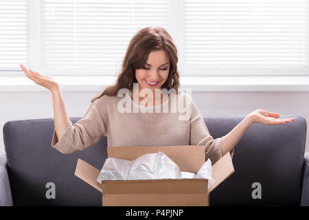 Smiling Young Woman Sitting on Sofa Déballage colis reçu Banque D'Images