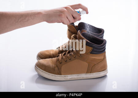 La main de l'homme déodorant propagation sur les chaussures malodorantes contre fond blanc Banque D'Images