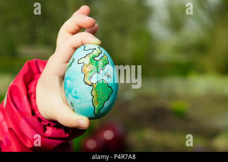 Enfant tenant un œuf avec la planète Terre peint sur elle lors d'une journée ensoleillée à l'extérieur. Banque D'Images