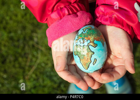 Enfant tenant un œuf avec la planète Terre peint sur elle lors d'une journée ensoleillée à l'extérieur. Banque D'Images