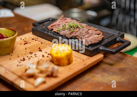 Plaque en fonte avec des tranches de bifteck de faux-filet grillés sur table avec des quartiers de pommes de terre jaunes et l'huile dans une soucoupe sur table avec copie espace Banque D'Images