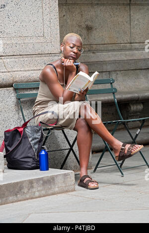 Une belle jeune femme lisant un livre avec un stylo dans sa main à l'extérieur de la succursale principale de la bibliothèque publique à Midtown Manhattan, New York City Banque D'Images