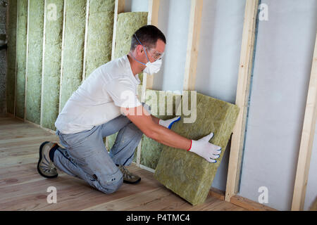 Travailleur dans des lunettes et un masque respiratoire l'isolation isolation laine de roche dans le cadre en bois pour les murs de maison pour barrière froide. Chaud confortable Banque D'Images