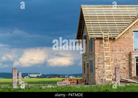 Maison à deux étages avec toit en bois en construction. À grande échelle en bois et de murs en briques rouges tas de briques. Concept de développement immobilier. Banque D'Images