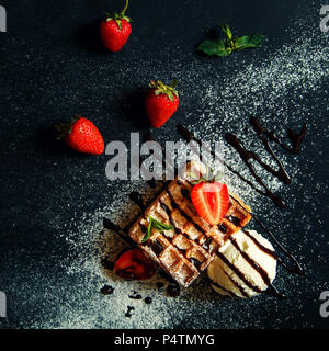 Gaufres Belges avec de la crème glacée et les fraises sur un fond noir. Banque D'Images