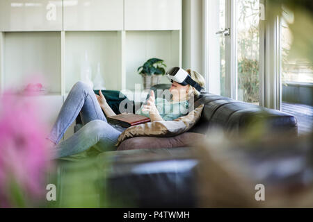 Femme allongée sur le canapé avec l'album photo à l'aide de lunettes de réalité virtuelle Banque D'Images