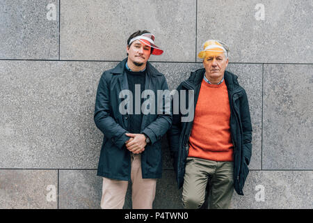 Portrait de jeune homme et senior man wearing pare-soleil, appuyé contre un mur Banque D'Images