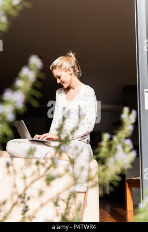 Smiling mature woman sitting at terrasse ouverte porte à l'aide d'ordinateur portable Banque D'Images
