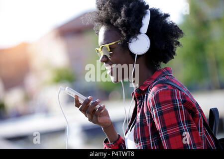 Portrait of laughing young woman using cell phone et écouteurs Banque D'Images