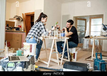 Heureux couple rénovation de télévision, faire une pause, de boire du vin lire Banque D'Images