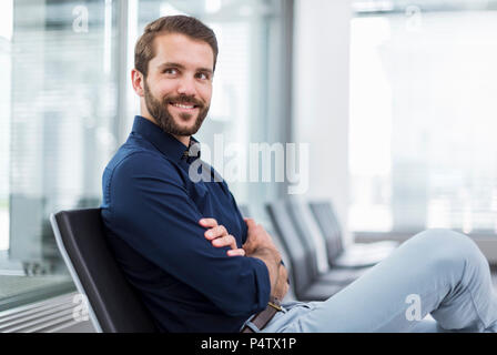 Smiling young businessman sitting in waiting area Banque D'Images