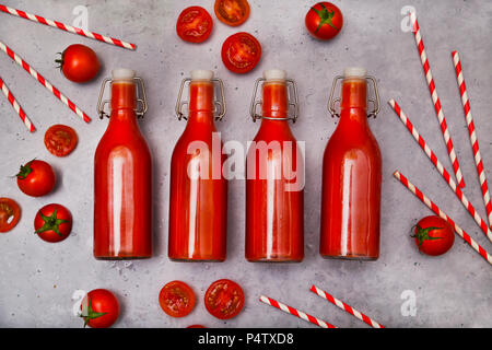 Rangée de quatre swing top bouteille de jus de tomate faite maison, les pailles et les tomates sur la masse grise Banque D'Images