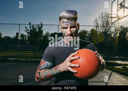 Portrait de jeune homme tatoué avec le basket-ball sur cour Banque D'Images