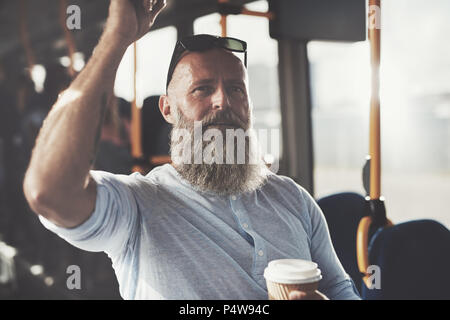 Homme mature avec une longue barbe et de boire une tasse de café à emporter en étant debout sur un bus pendant son trajet du matin Banque D'Images