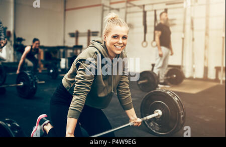 Smiling young woman in sportswear prépare à soulever des poids pendant une séance d'exercices dans une salle de sport Banque D'Images