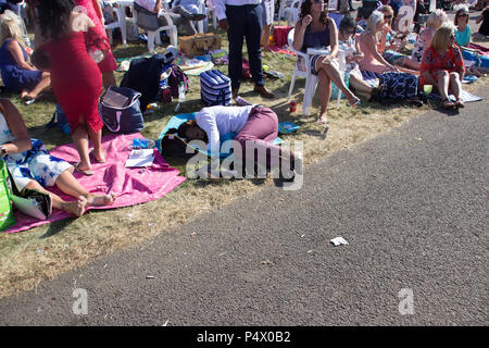 Man in suit jette recroquevillée sur l'herbe dans une foule de personnes au Royal Ascot. Il tient sa tête comme s'pas bien Banque D'Images