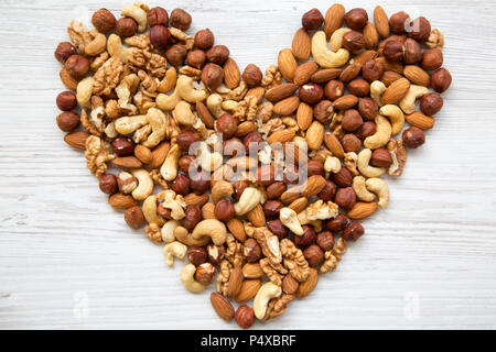 Modèle d'écrous en forme coeur. Noix de cajou, noisettes, noix, amandes sur fond de bois blanc, vue du dessus. Mise à plat. Banque D'Images