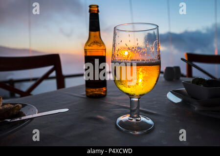 Verre de bière sur une table de restaurant sur la mer au coucher du soleil sur l'île d'El Hierro, Îles Canaries, Espagne Banque D'Images